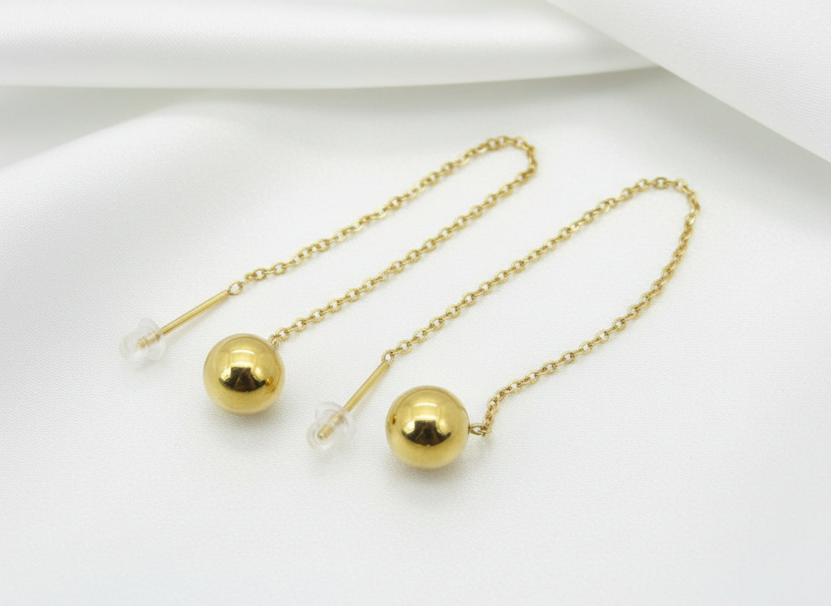 Gold earrings with spherical beads on a plain background