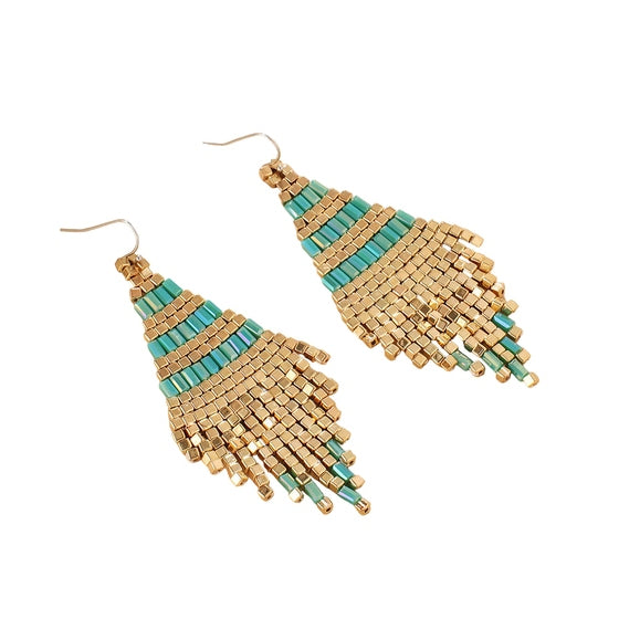 Gold and turquoise beaded earrings on a beige surface