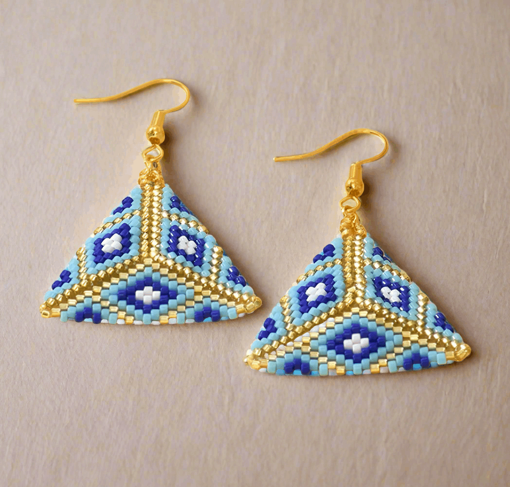 Pair of geometrically designed earrings with blue and gold colors on a beige background