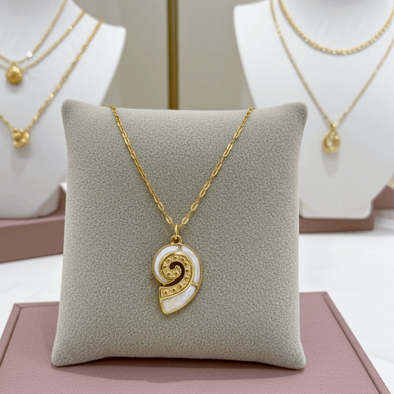 Gold necklace with a decorative pendant on a gray cushion, with more necklaces in the background.