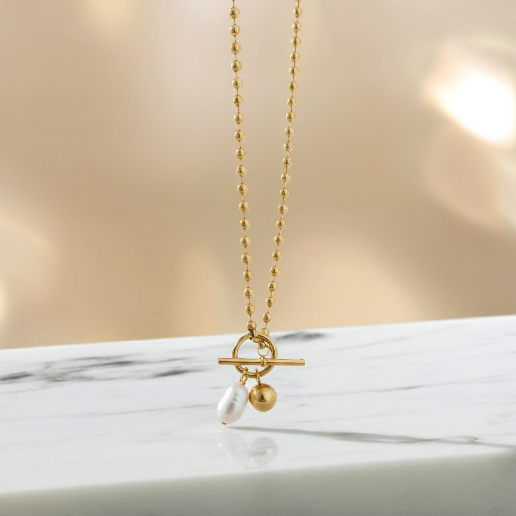 Gold necklace with a pearl pendant on a marble surface