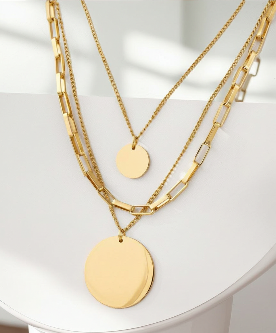 Three gold necklaces with round pendants on a white surface