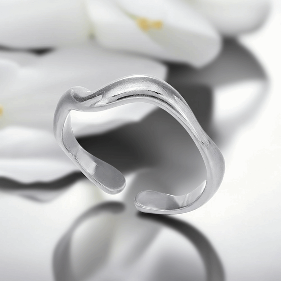 Silver ring with a wavy design on a reflective surface