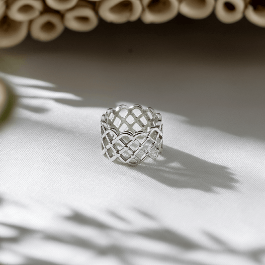 Silver woven ring on a light fabric background with natural light casting shadows