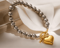 Silver beaded bracelet with a gold heart charm on a white surface