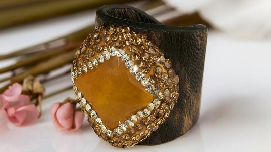 Decorative ring with wooden base and goldstone center on a white surface with flowers and leaves.