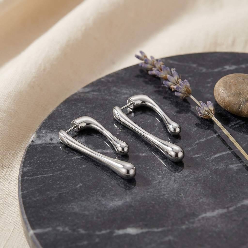 Silver earrings on a dark stone surface with lavender and a stone.