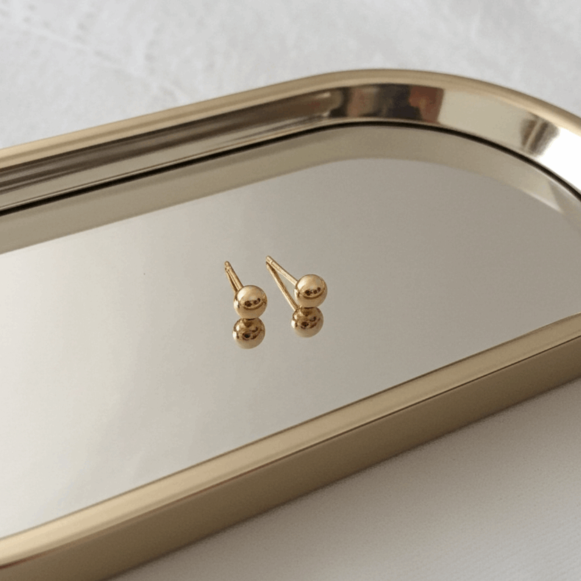 Gold earrings on a reflective gold tray with a white background