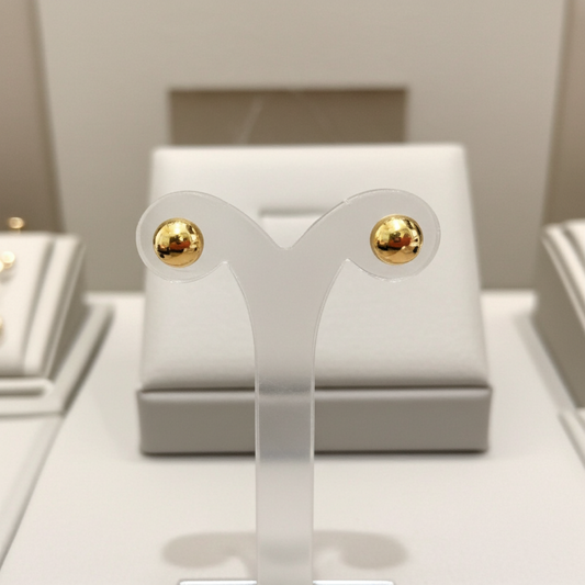 Gold earrings on a white earring stand with a neutral background