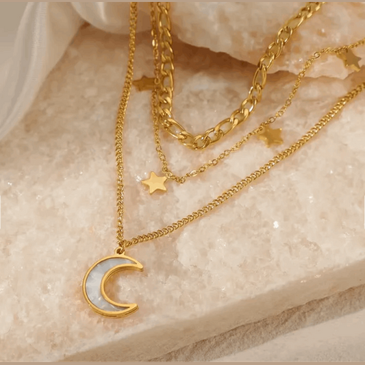 Gold necklaces with moon and star pendants on a textured surface