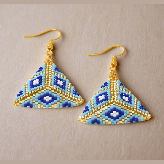 Pair of geometrically designed earrings with blue and gold colors on a beige background