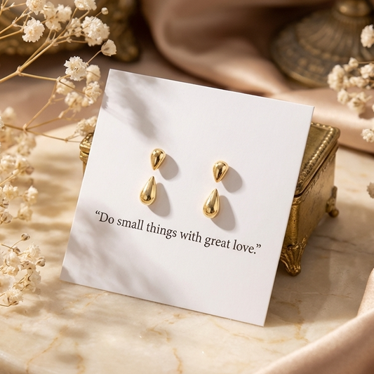 Gold earrings on a card with text, surrounded by white flowers on a marble surface.