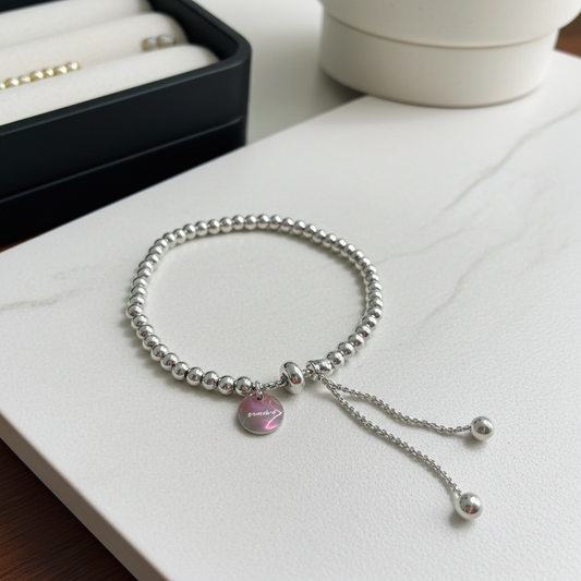 Silver bracelet with a silver round-shaped charm on a white surface