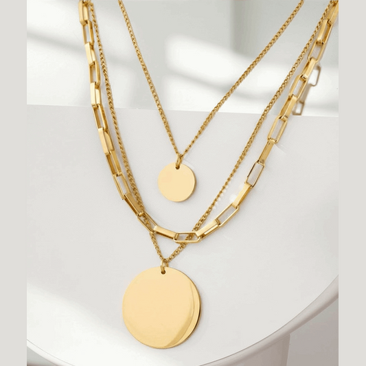 Three gold necklaces with round pendants on a white surface