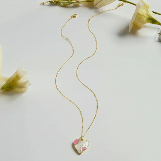 Gold necklace with a heart-shaped pendant on a light gray background with flowers.