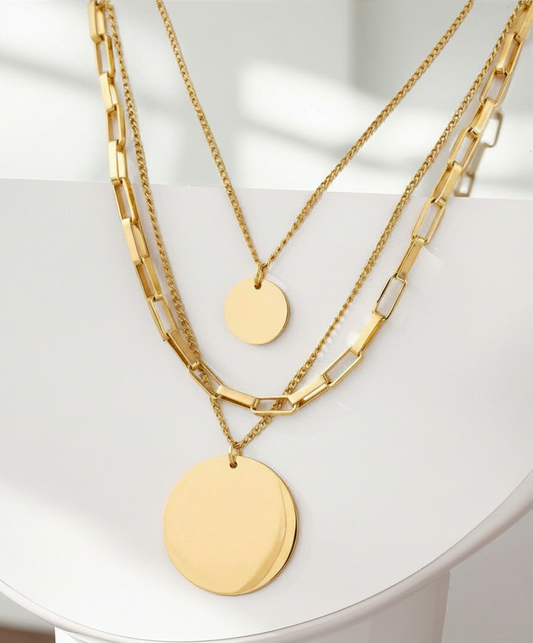 Three gold necklaces with round pendants on a white surface