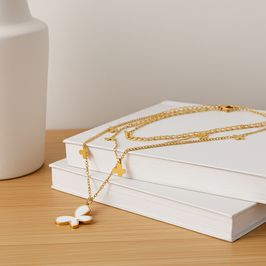 Gold necklaces with butterfly and cross pendants on a stack of white books.